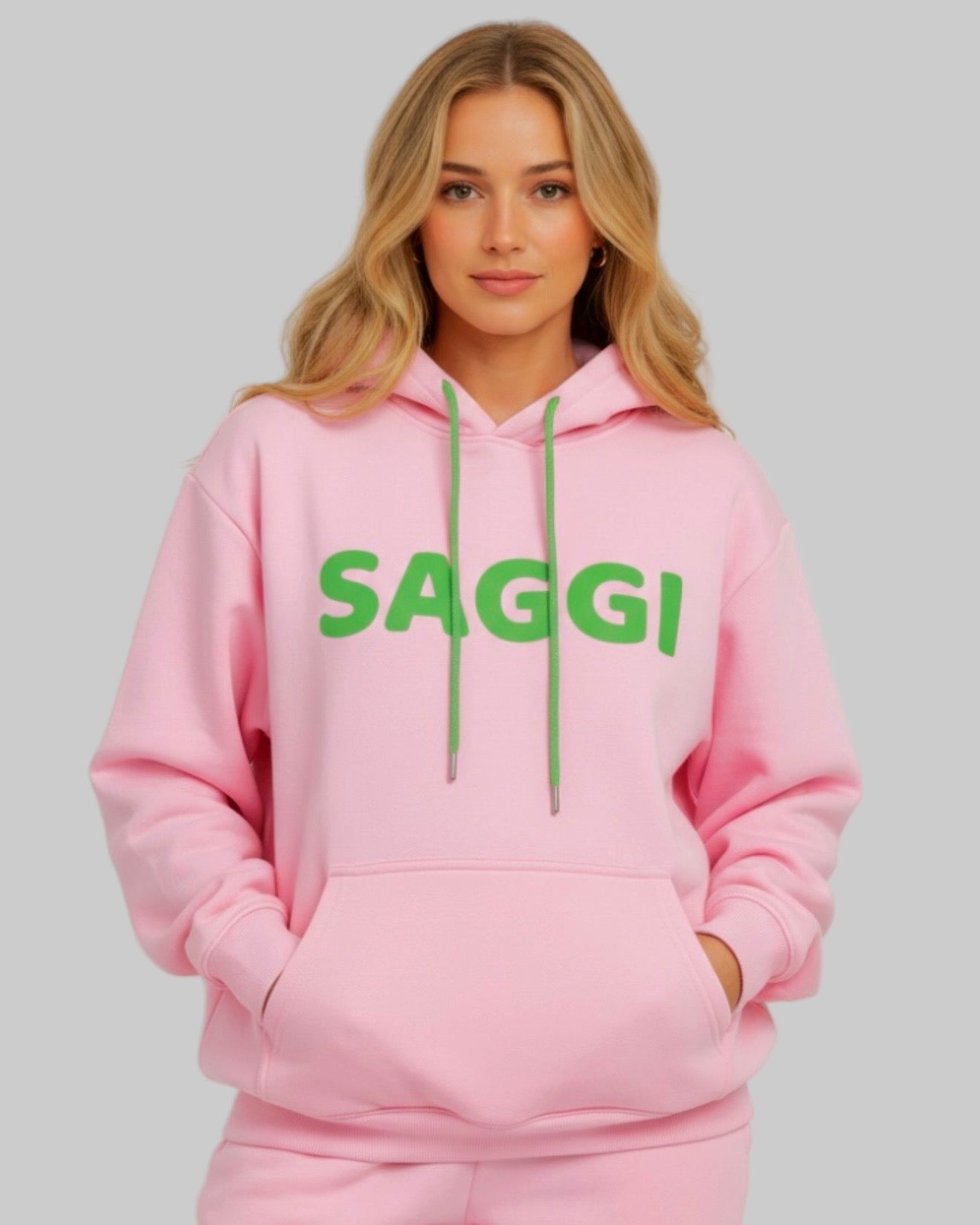 Model wearing pink SAGGI heavyweight graphic hoodie with green logo and green drawstrings, true-to-size fit.