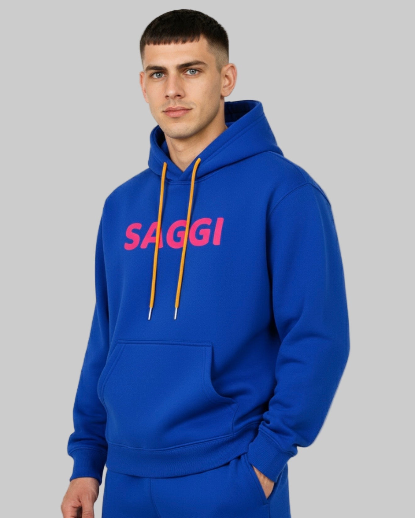 Model wearing royal blue SAGGI heavyweight graphic hoodie with fuchsia logo and orange drawstrings, true-to-size fit.