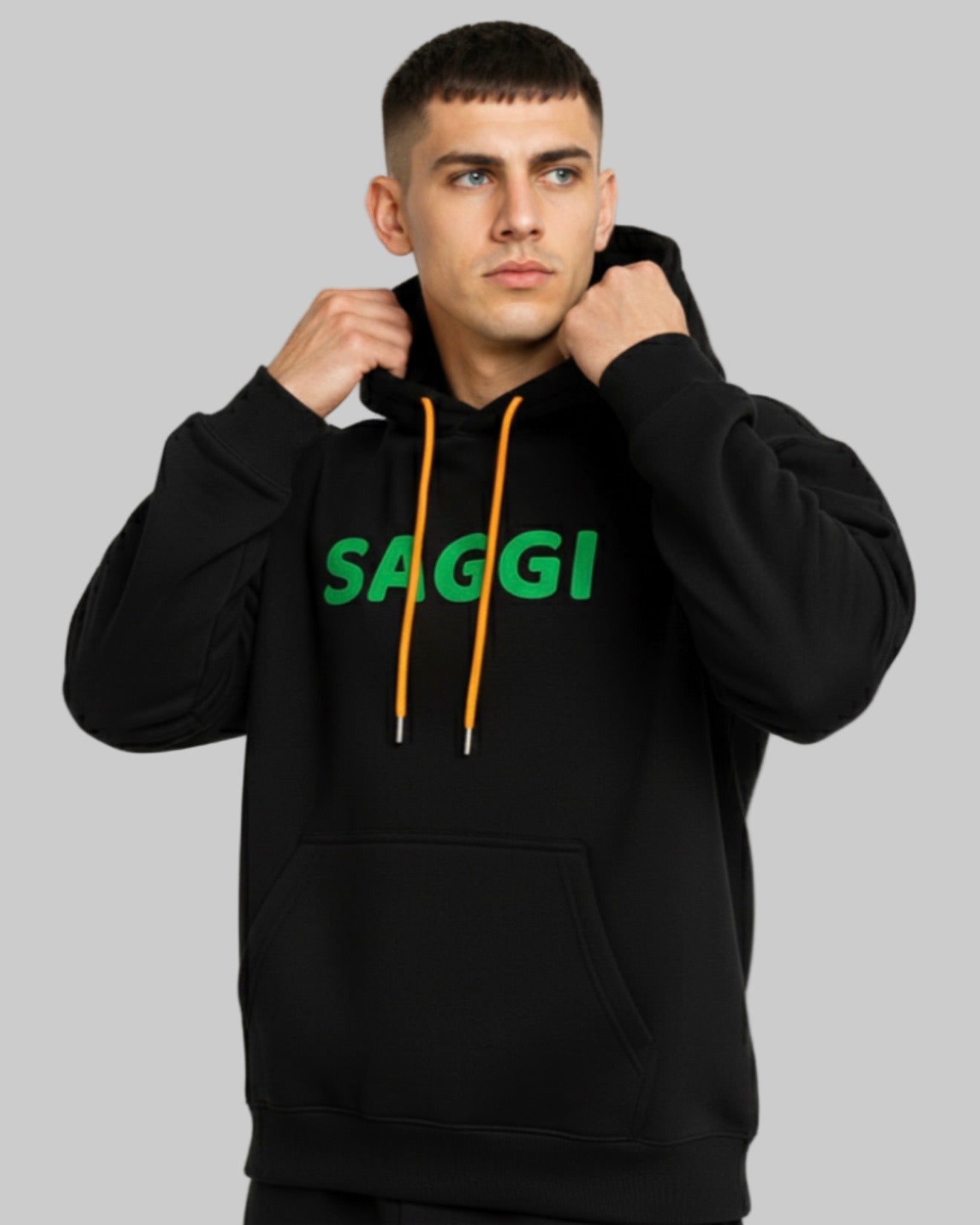 Model wearing black SAGGI heavyweight graphic hoodie with green logo and orange drawstrings, true-to-size fit.