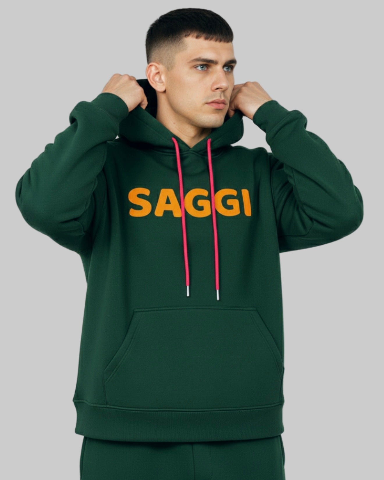 Model wearing forest green SAGGI heavyweight graphic hoodie with orange logo and fuchsia drawstrings, true-to-size fit.