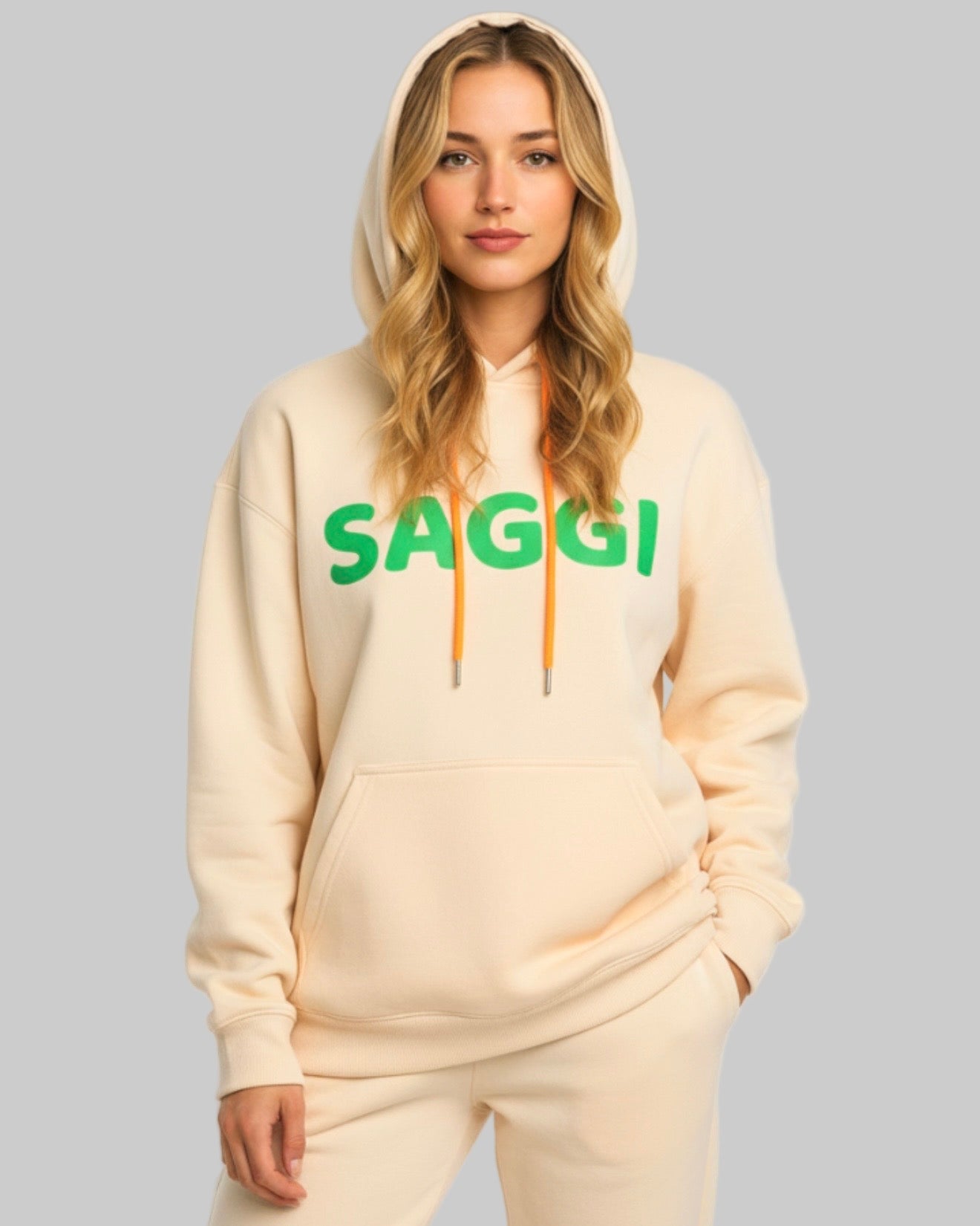 Model wearing khaki SAGGI heavyweight graphic hoodie with green logo and orange drawstrings, true-to-size fit.
