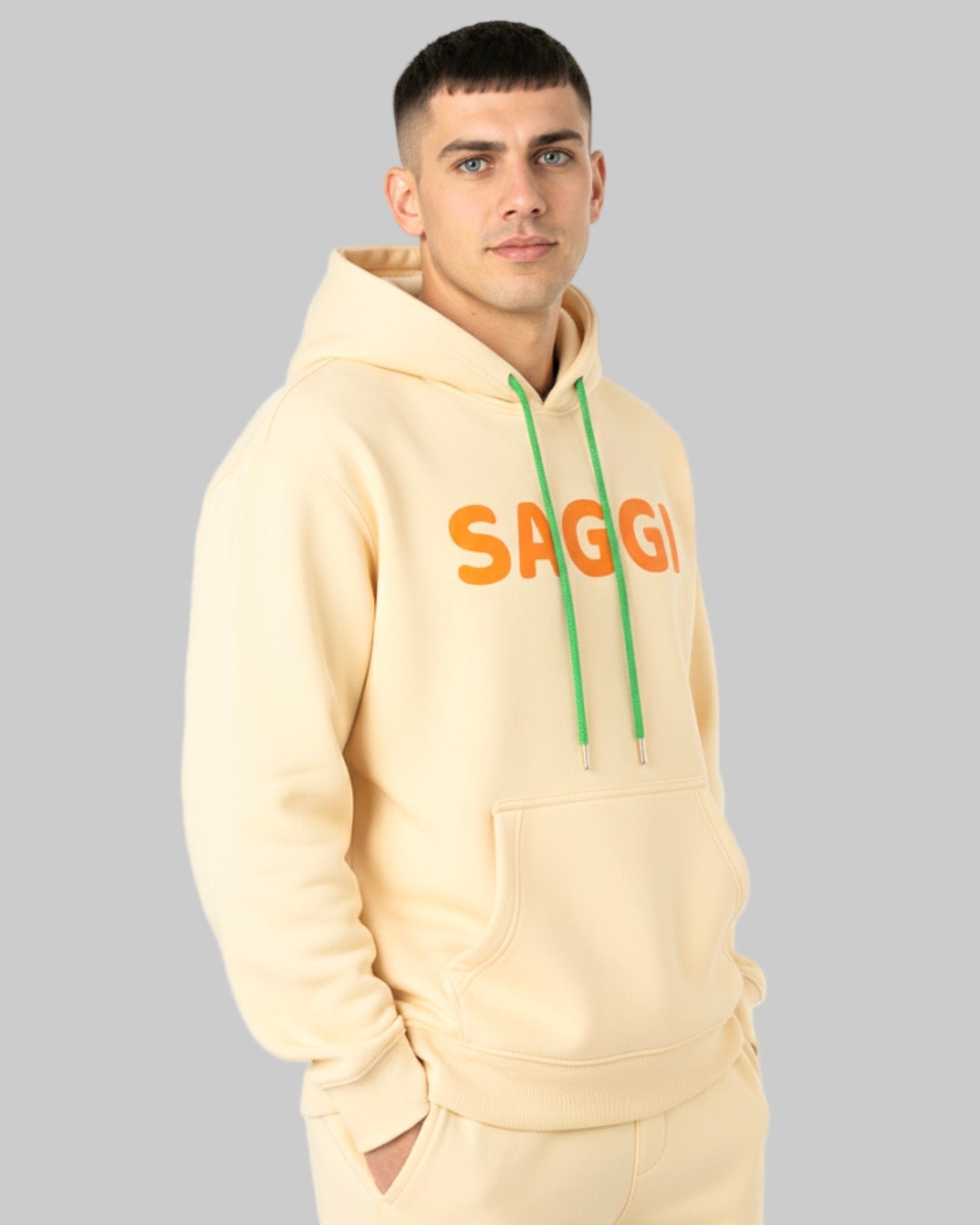 Model wearing khaki SAGGI heavyweight graphic hoodie with orange logo and green drawstrings, true-to-size fit.