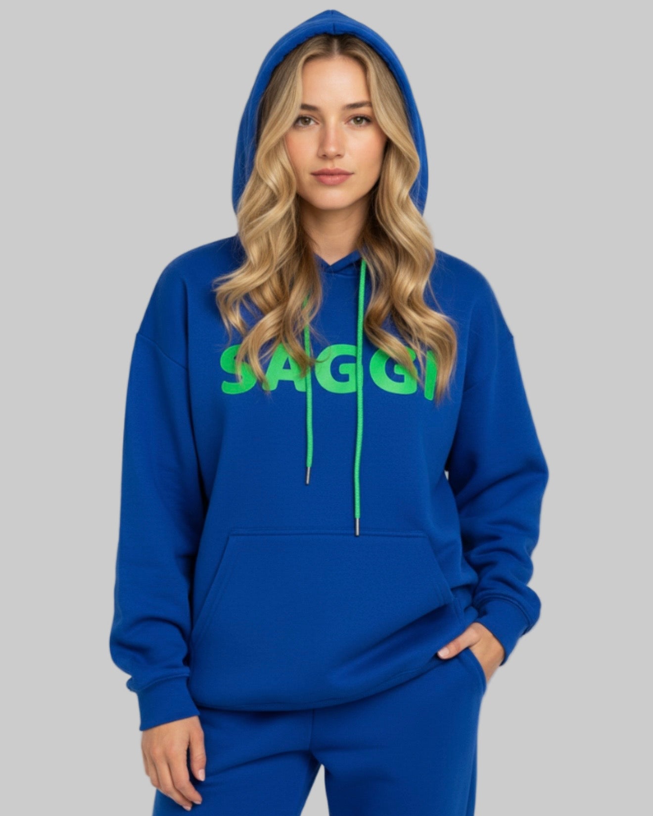 Model wearing royal blue SAGGI heavyweight graphic hoodie with green logo and green drawstrings, true-to-size fit.