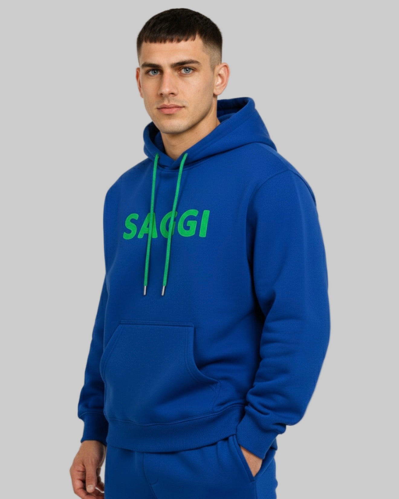 Model wearing royal blue SAGGI heavyweight graphic hoodie with green logo and green drawstrings, true-to-size fit.