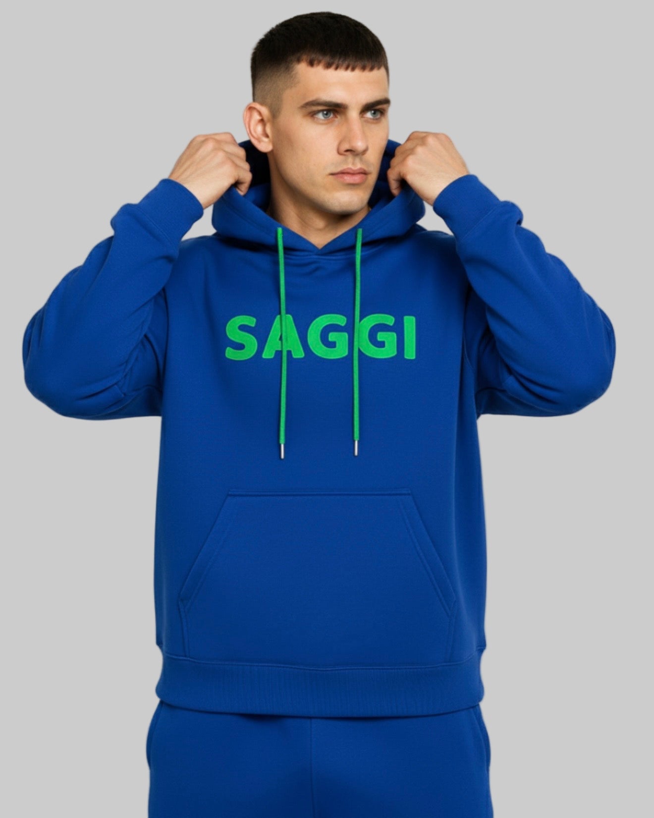 Model wearing royal blue SAGGI heavyweight graphic hoodie with green logo and green drawstrings, true-to-size fit.